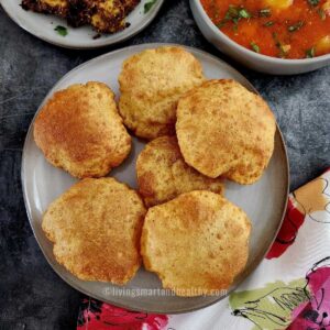 bedmi puri on a plate with aloo tamatar sabzi on the side