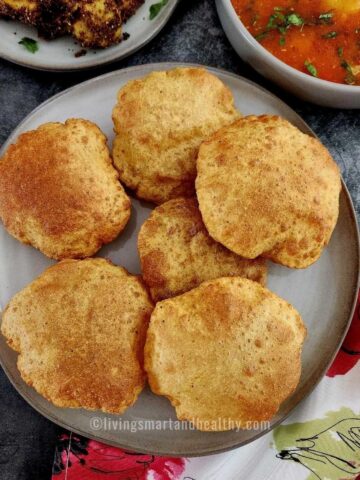 bedmi puri on a plate with aloo tamatar sabzi on the side