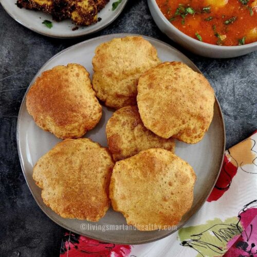 bedmi puri on a plate with aloo tamatar sabzi on the side