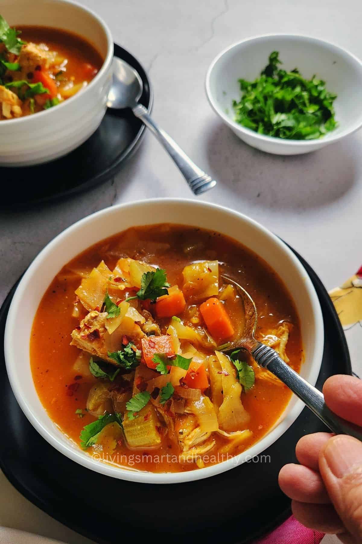 Ladle serving hearty chicken and cabbage soup into a bowl