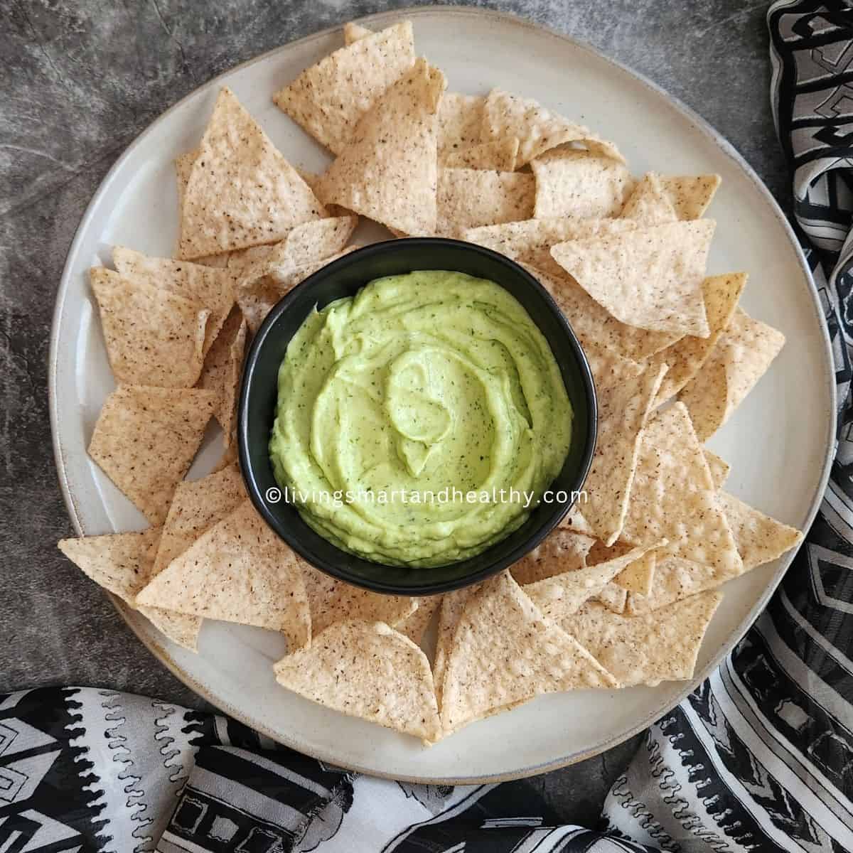 Fresh ingredients for easy avocado dip recipe laid out on a wooden board - ripe avocados, lime, jalapeno, garlic, cilantro, mint, and Greek yogurt
