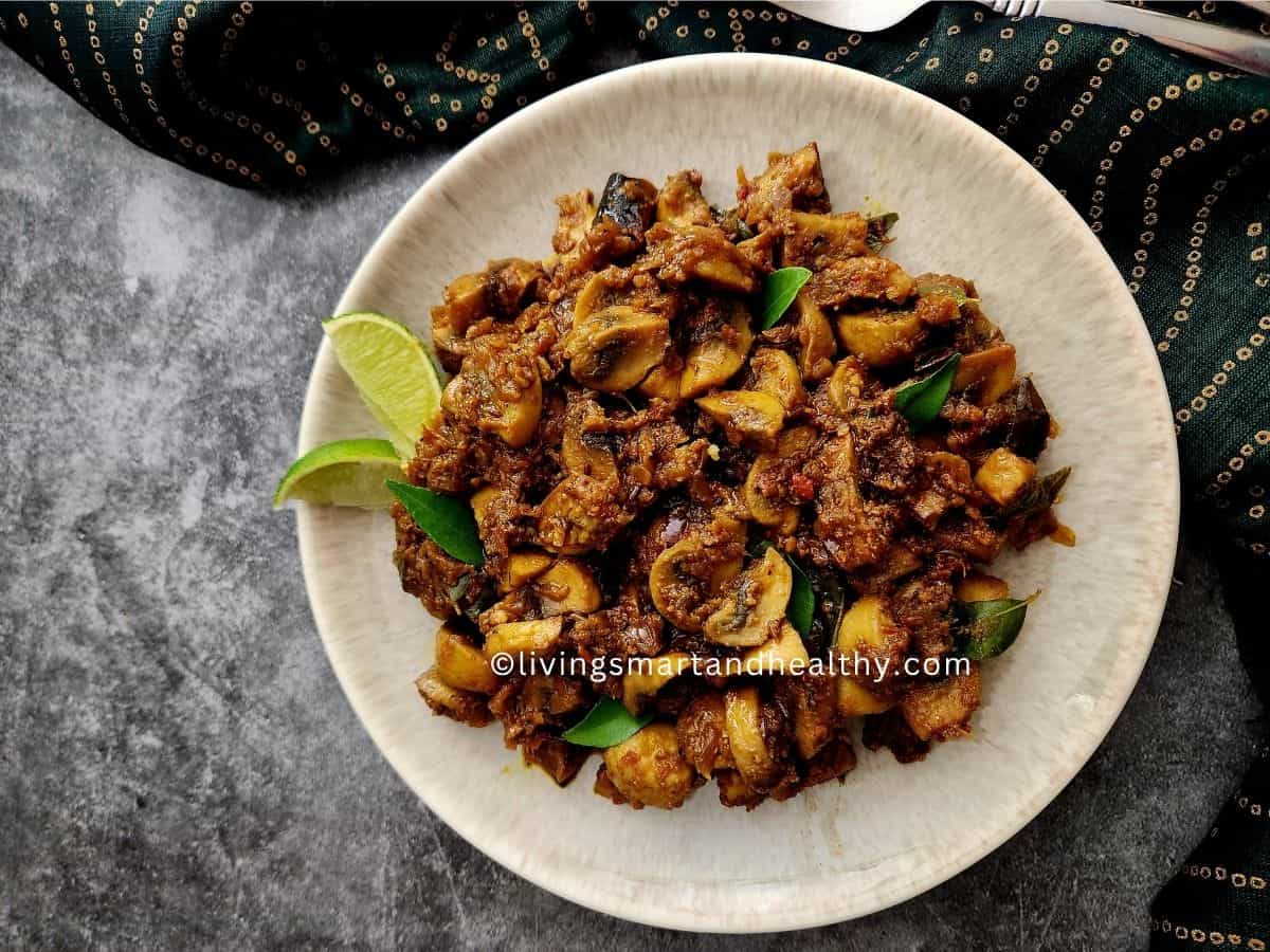 South Indian mushroom pepper fry in a black kadai with curry leaves and cracked black pepper