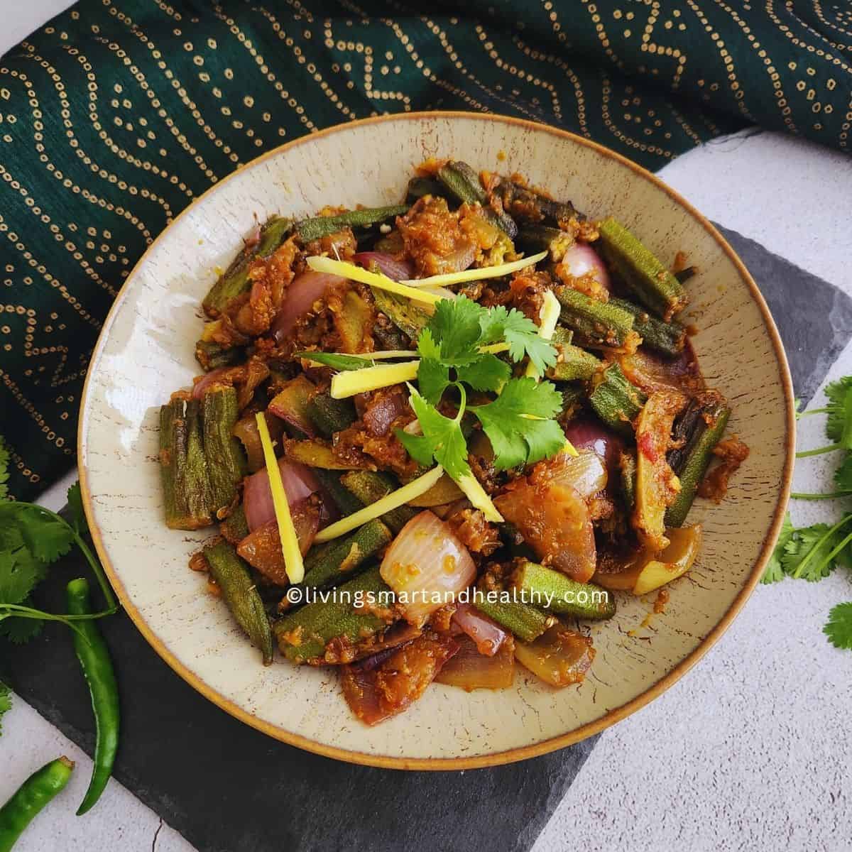 Bhindi Do Pyaza plated on a white dish with a side of phulka roti and sliced green chili garnish, shot from above