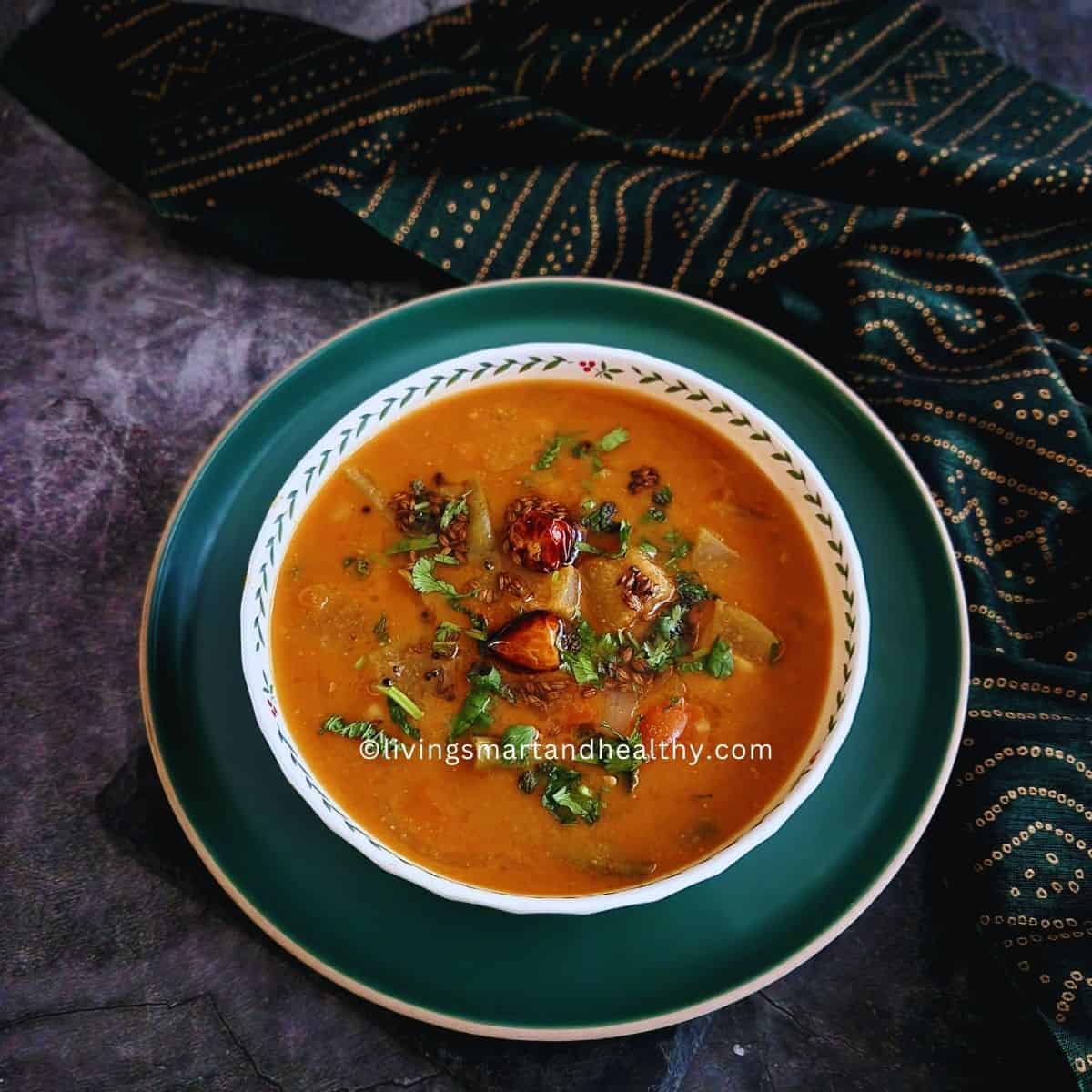 Close up of homemade sambar with drumstick, carrot, and okra in a rich tamarind lentil broth