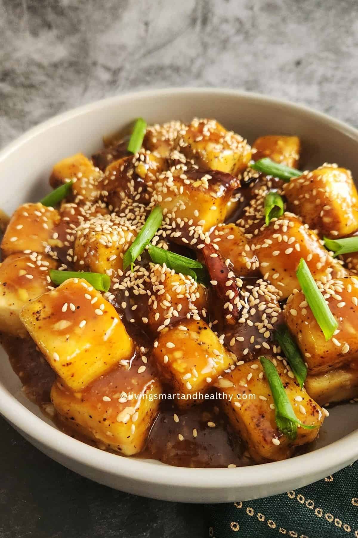 Easy vegan teriyaki tofu rice bowl with crispy tofu, steamed white rice, sesame seeds and sliced scallions in a white bowl