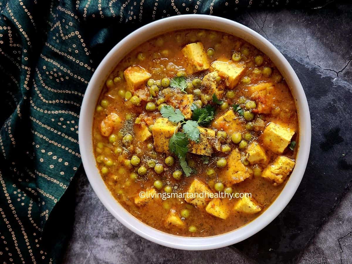 A bowl of vegan matar paneer with golden tofu cubes and green peas in a rich tomato-based curry, garnished with fresh cilantro