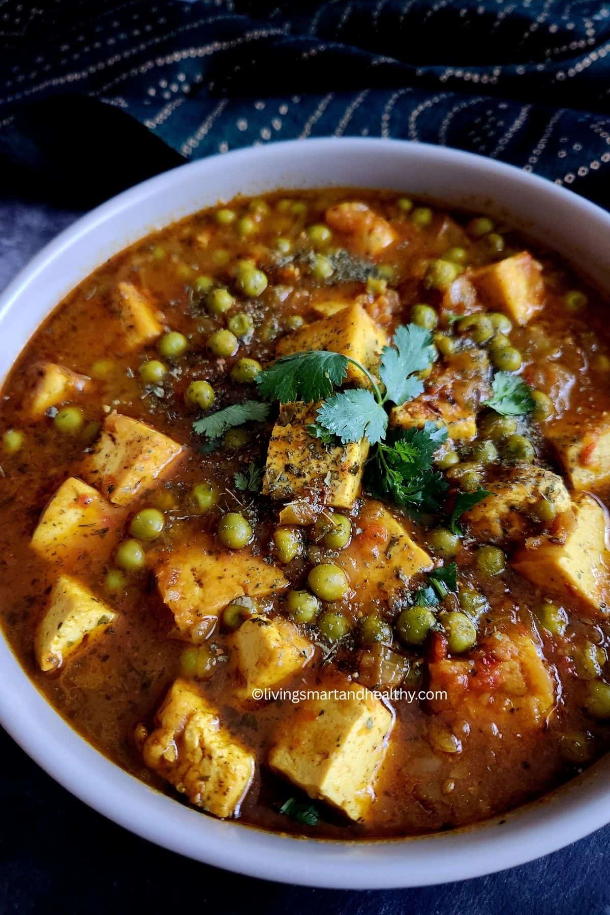 Vegan matar tofu curry served in a dark bowl with naan and jeera rice on the side
