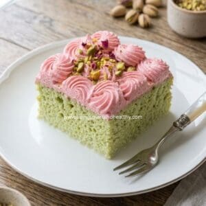 Slice of eggless paan tres leches cake topped with rose whipped cream and candied fennel on a white plate