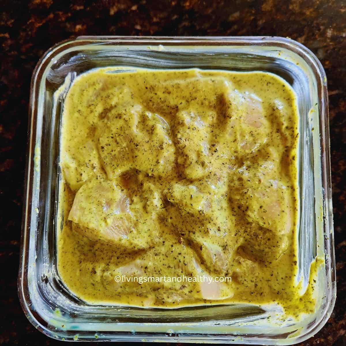 Boneless chicken pieces coated in thick green hariyali marinade with bell peppers and onions in a bowl