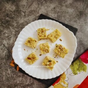 Kalakand squares topped with pistachios and saffron on a plate