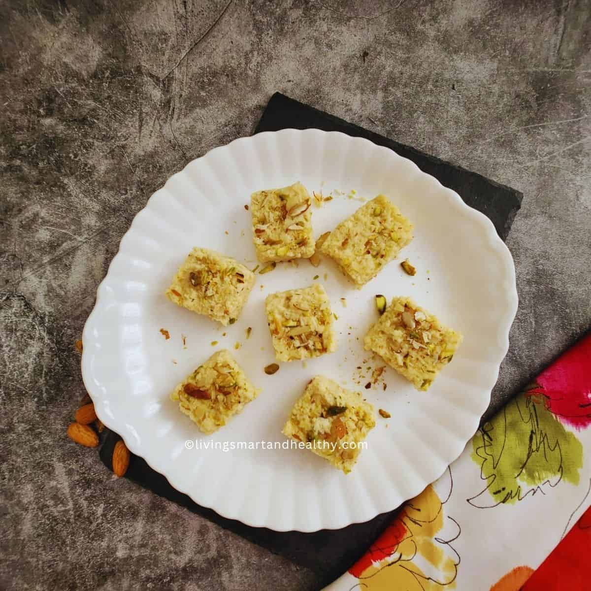 Kalakand squares topped with pistachios and saffron on a plate